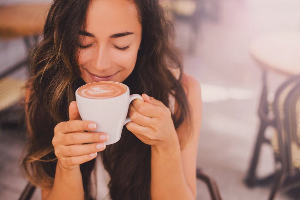 Young beautiful happy woman with long curly hair enjoying cappuccino in a street cafe